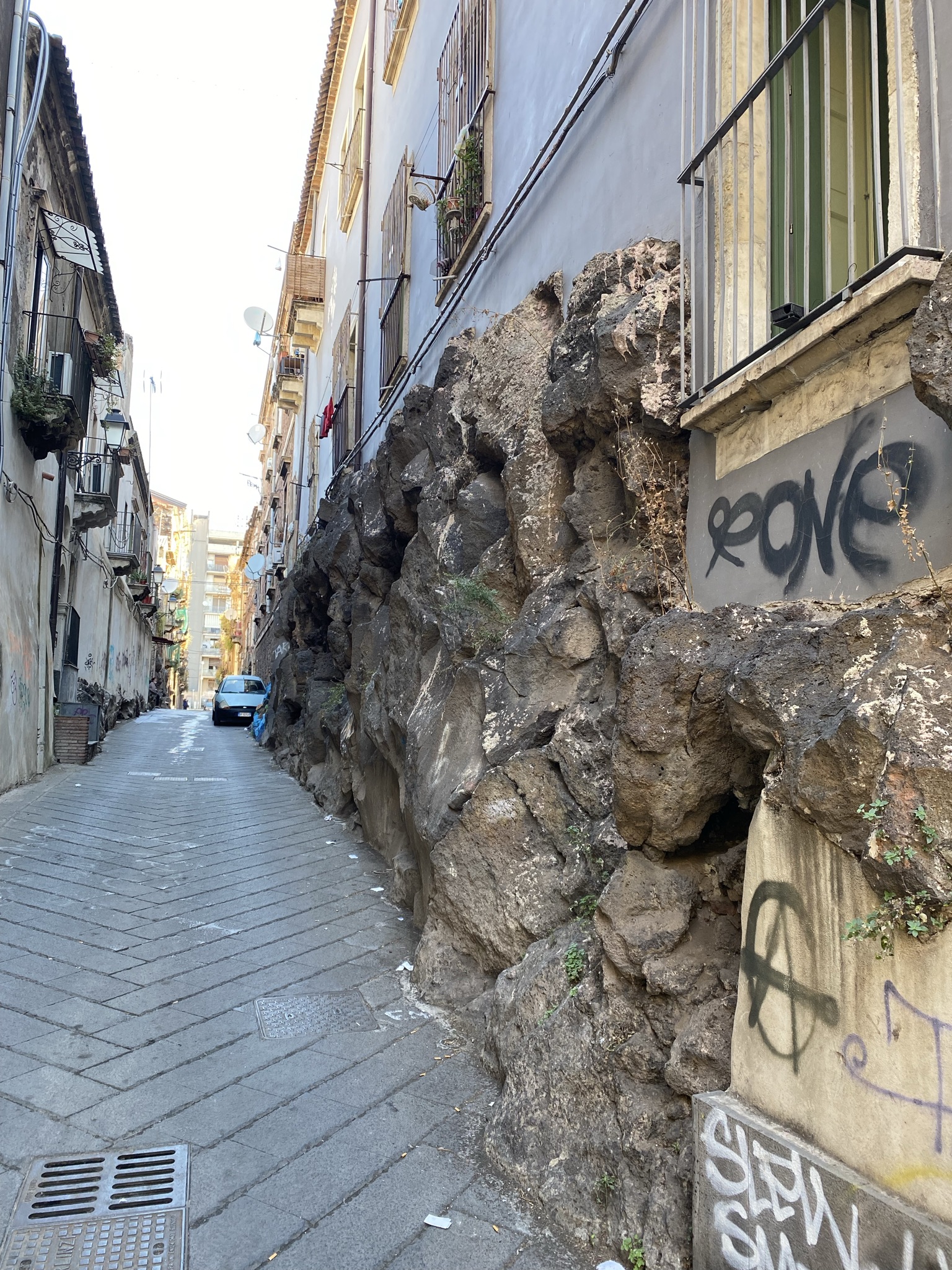 Narrow Catania street with lava rock wall from Mount Etna embedded into historic building facade