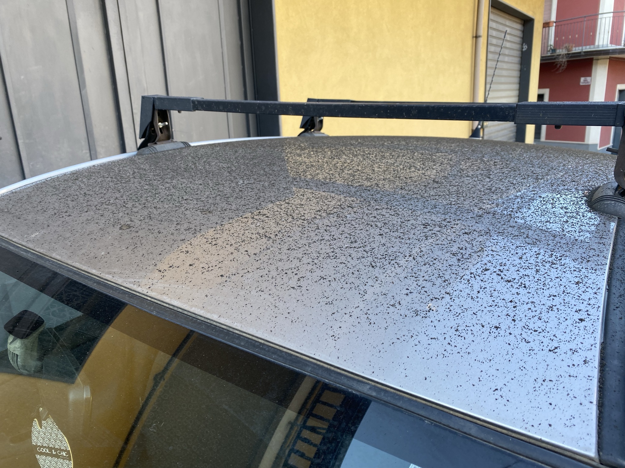 Car roof covered in fine black volcanic ash from Mount Etna, a common sight near Sicily's active volcano.