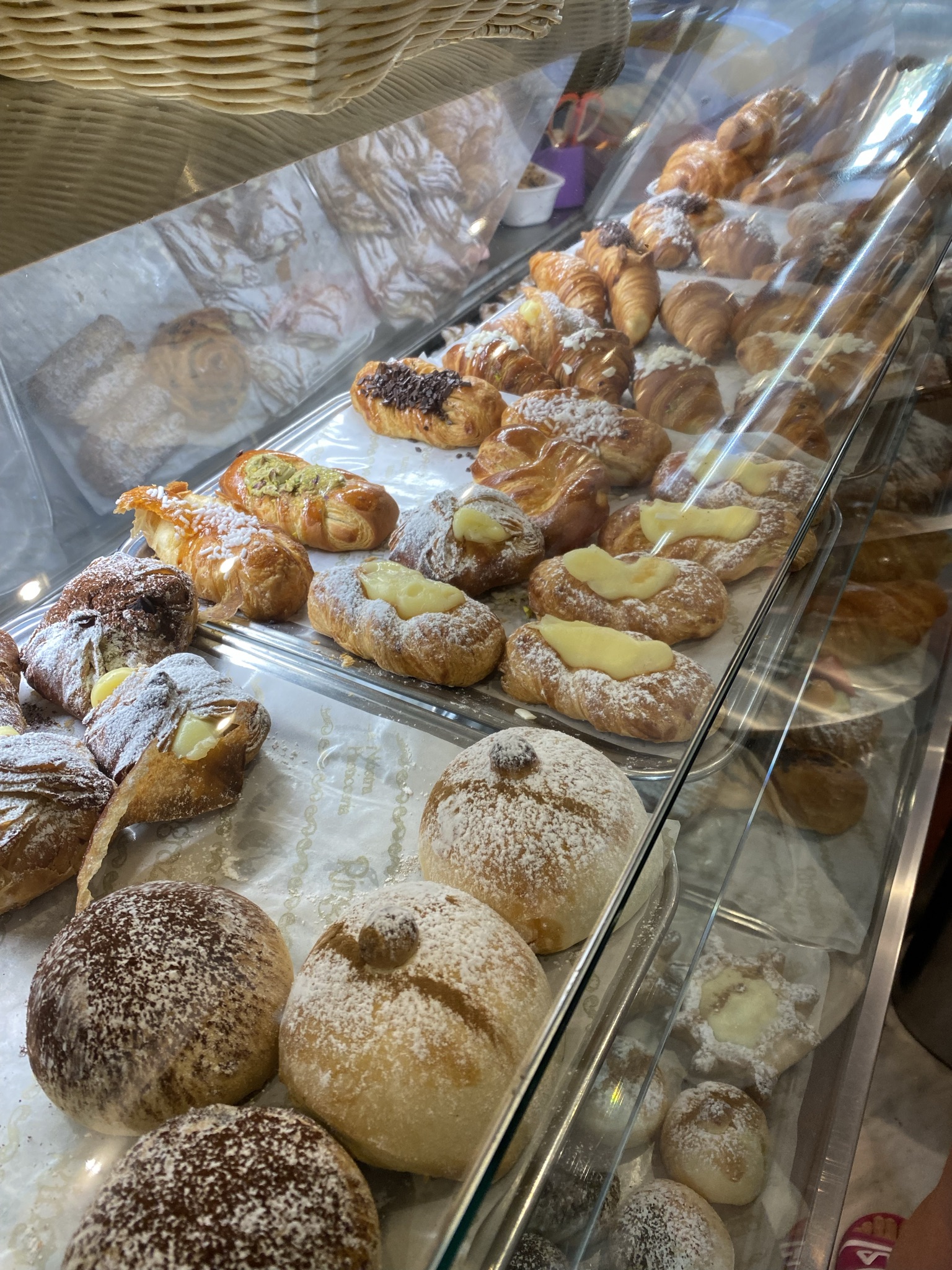 Sicilian pastry display case with zeppole, cornetti, and cream-filled sfogliatelle at a local bakery