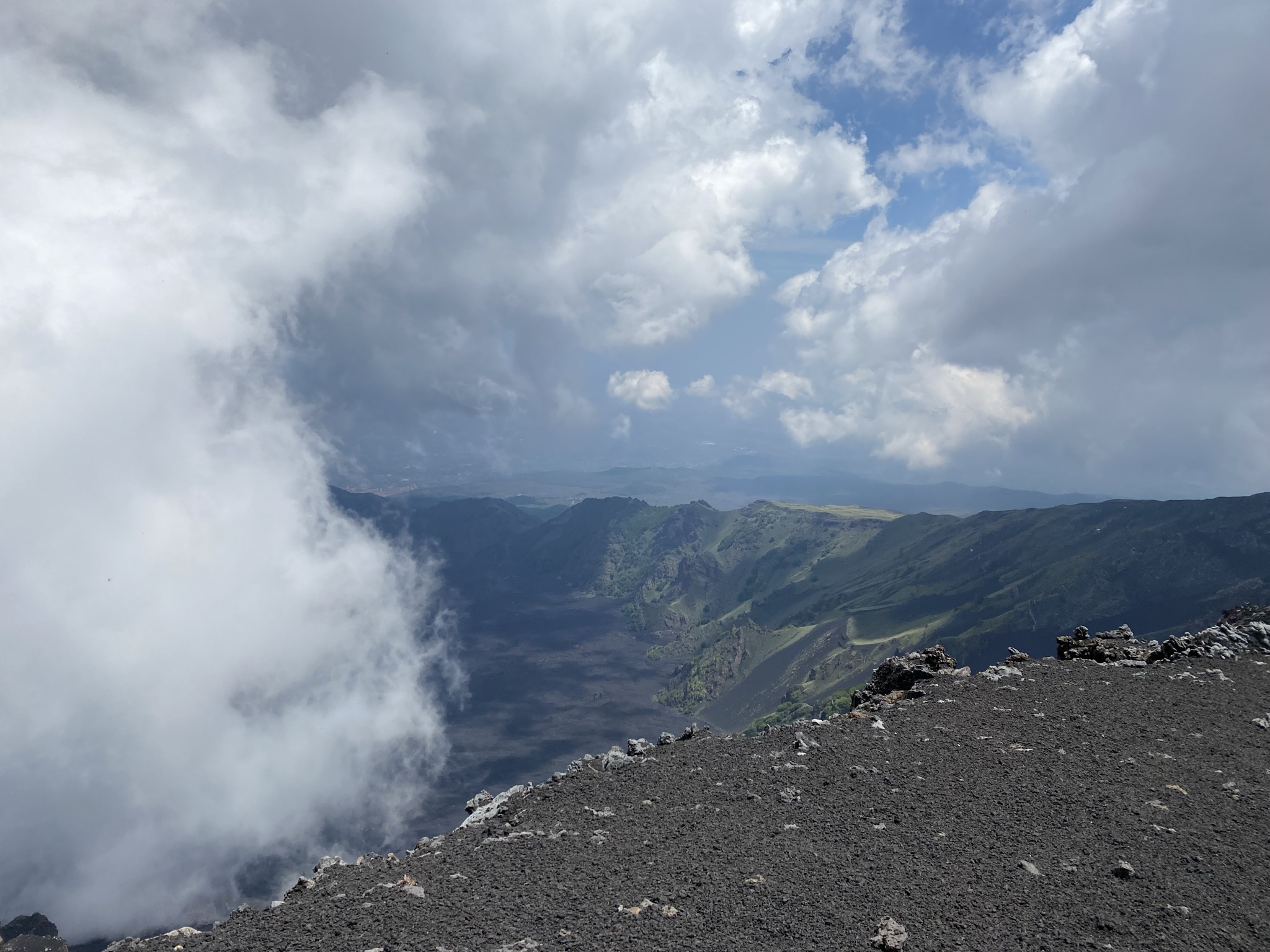 Panoramic view from Mount Etna summit, volcanic ash terrain and rising steam over Sicily's valleys below