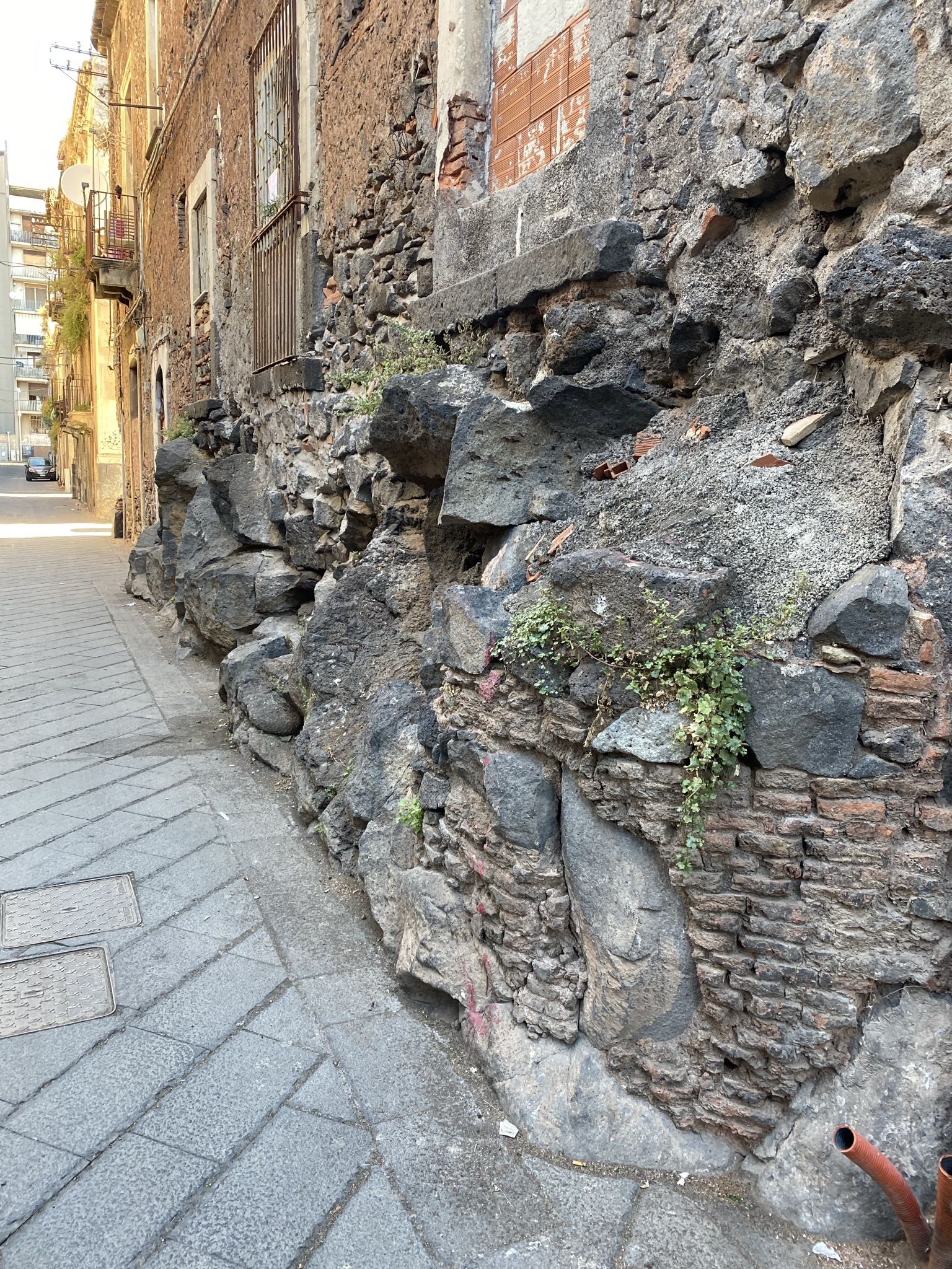 Ancient lava stone wall in Catania, showing dark volcanic basalt from Mount Etna embedded in historic street architecture