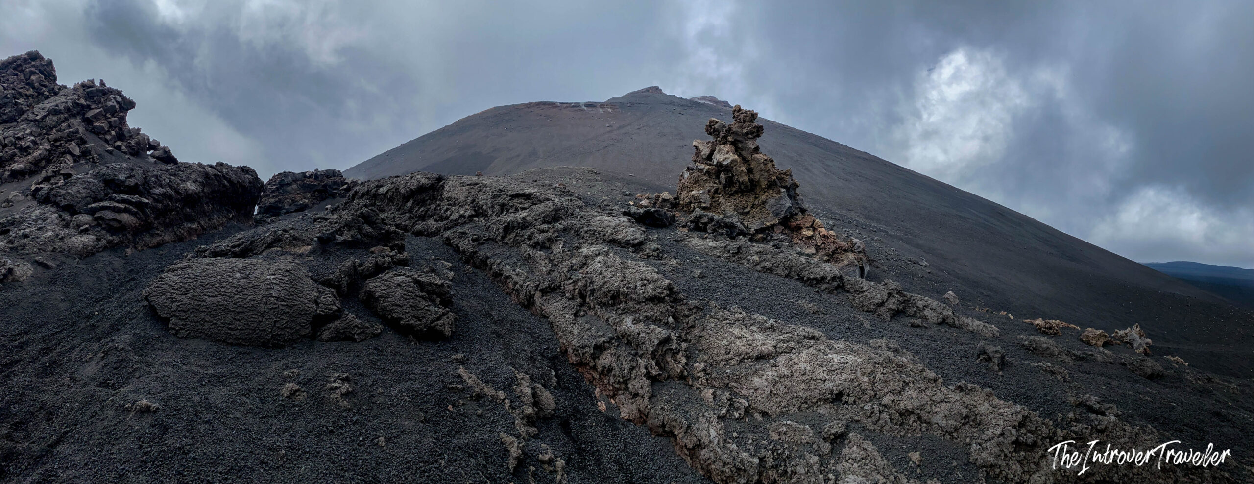 Jagged hardened lava fields on the slopes of Mount Etna, with the volcanic summit cone rising under stormy skies