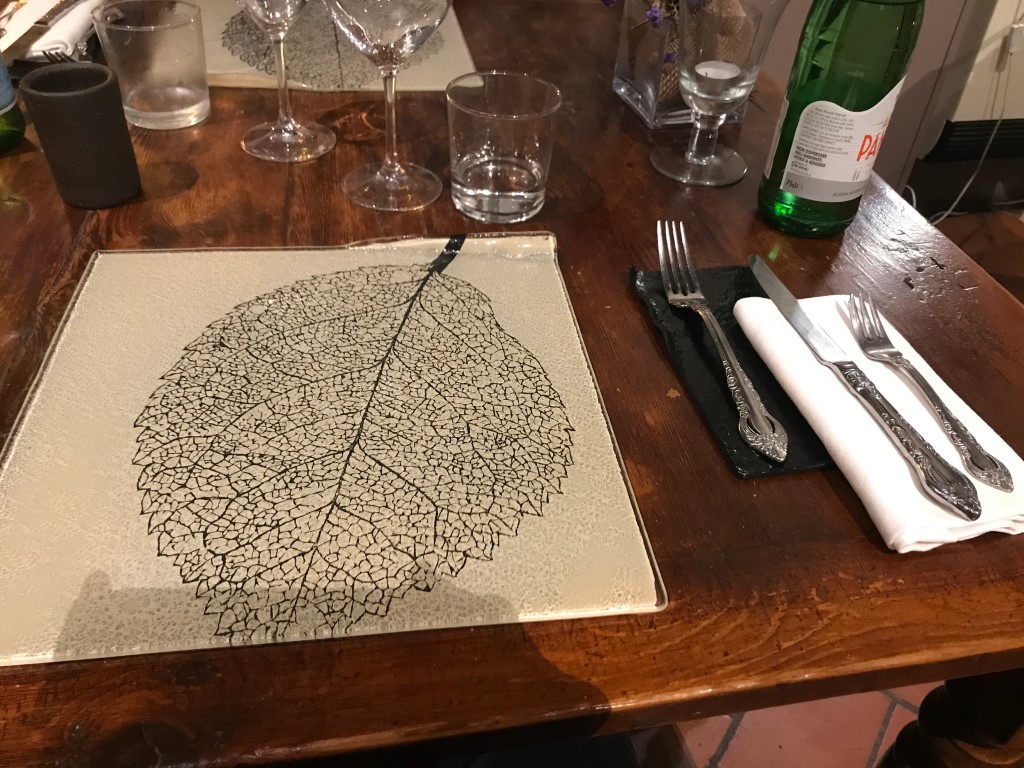 Elegant table setting at Osteria I'Ciocio, featuring a glass plate with leaf print design