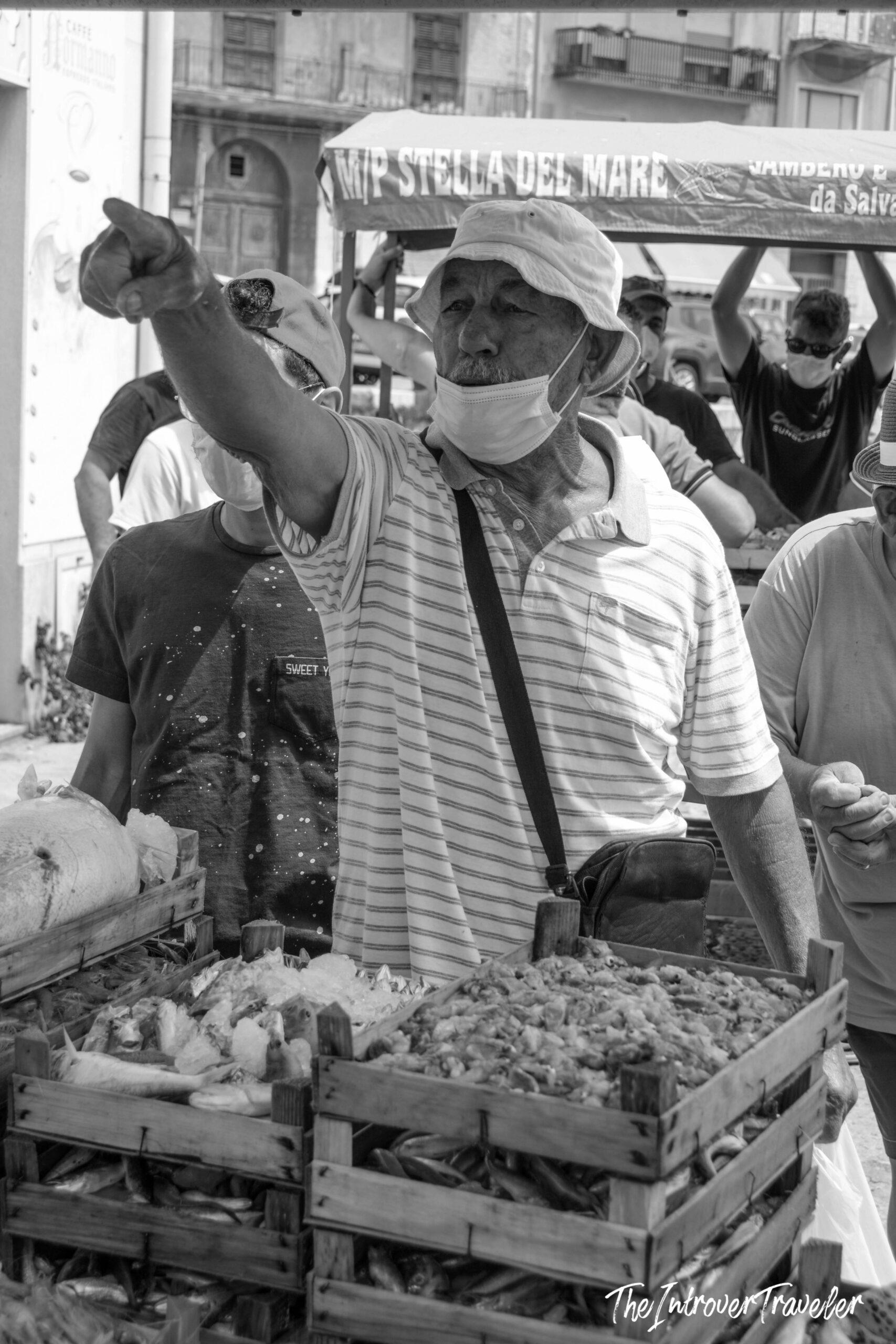 Vendor at Stella del Mare fish market gesturing over wooden crates of fresh seafood