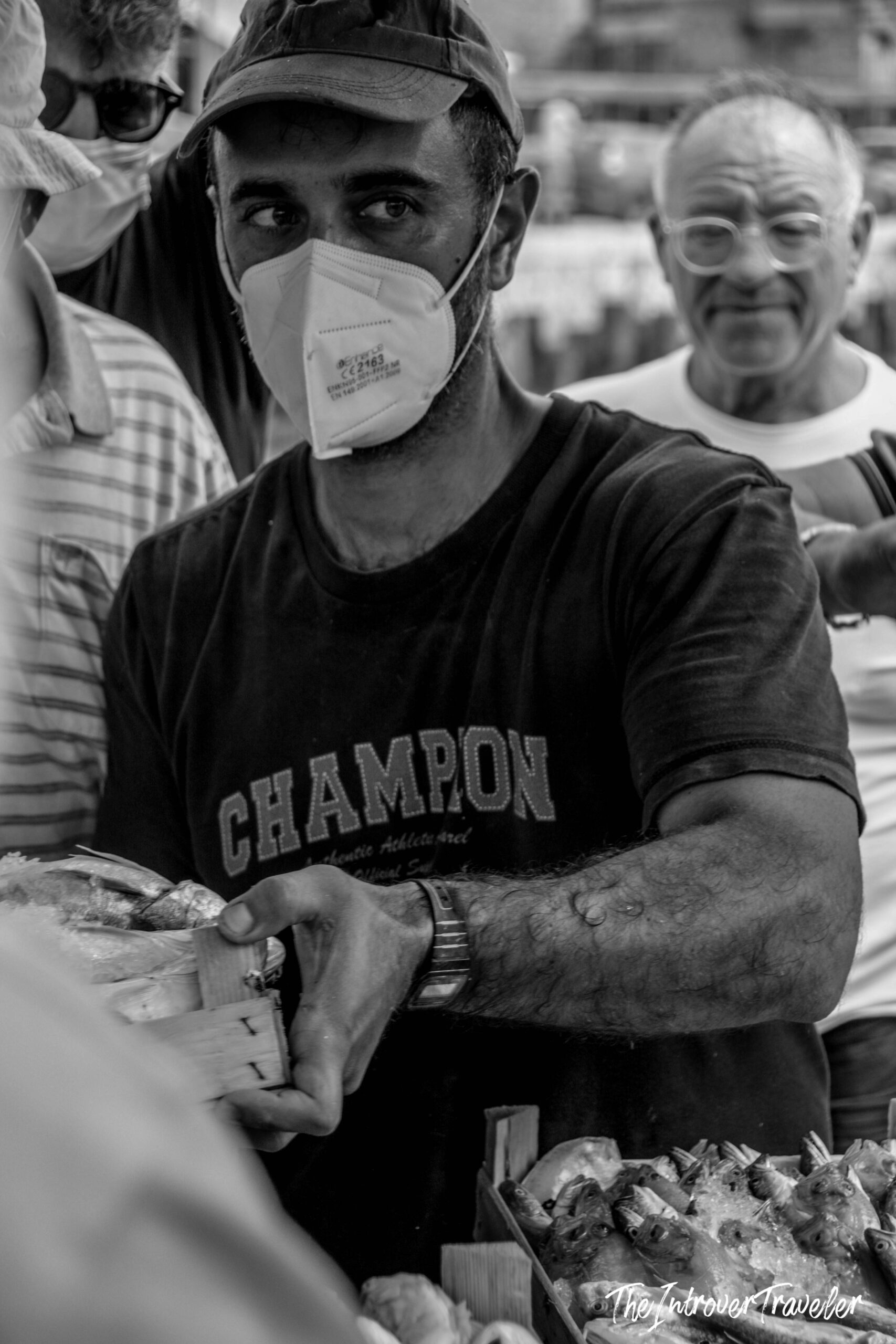 Masked fish vendor handling fresh seafood at a bustling coastal city fish market