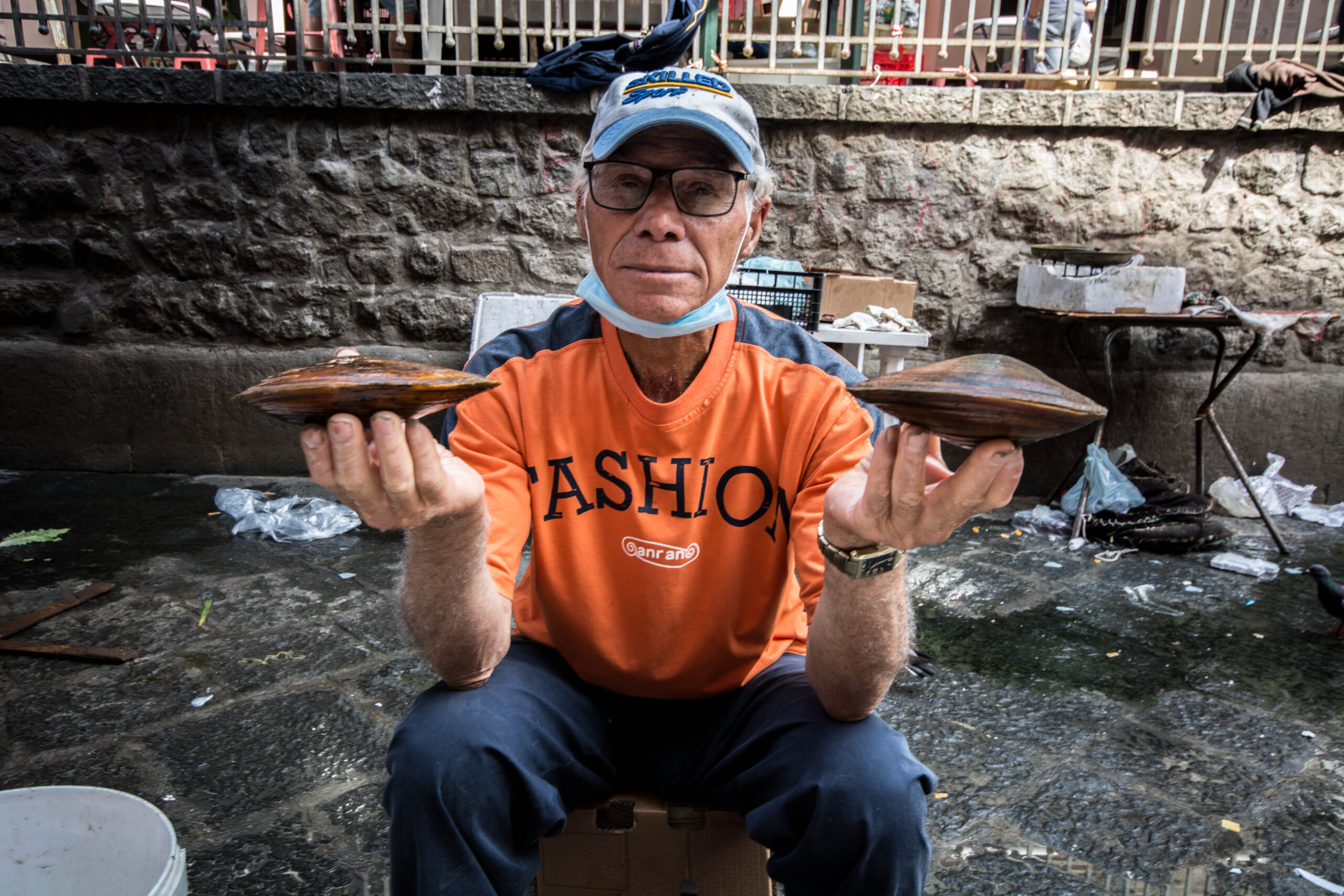 Vendor at a coastal fish market proudly displaying two large fresh mussels for sale
