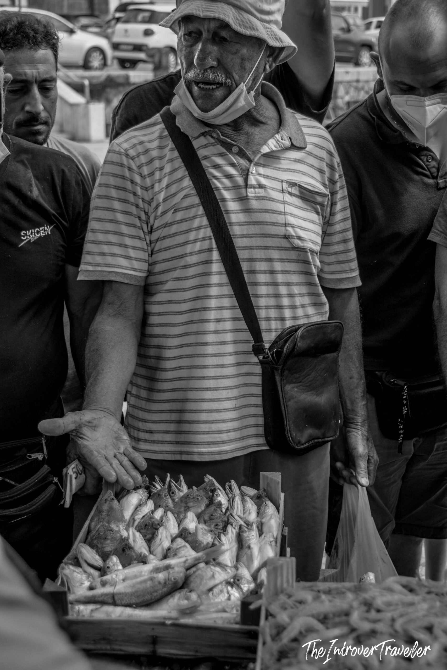 Fish vendor selling fresh catch at a bustling coastal city fish market, mask lowered mid-sale