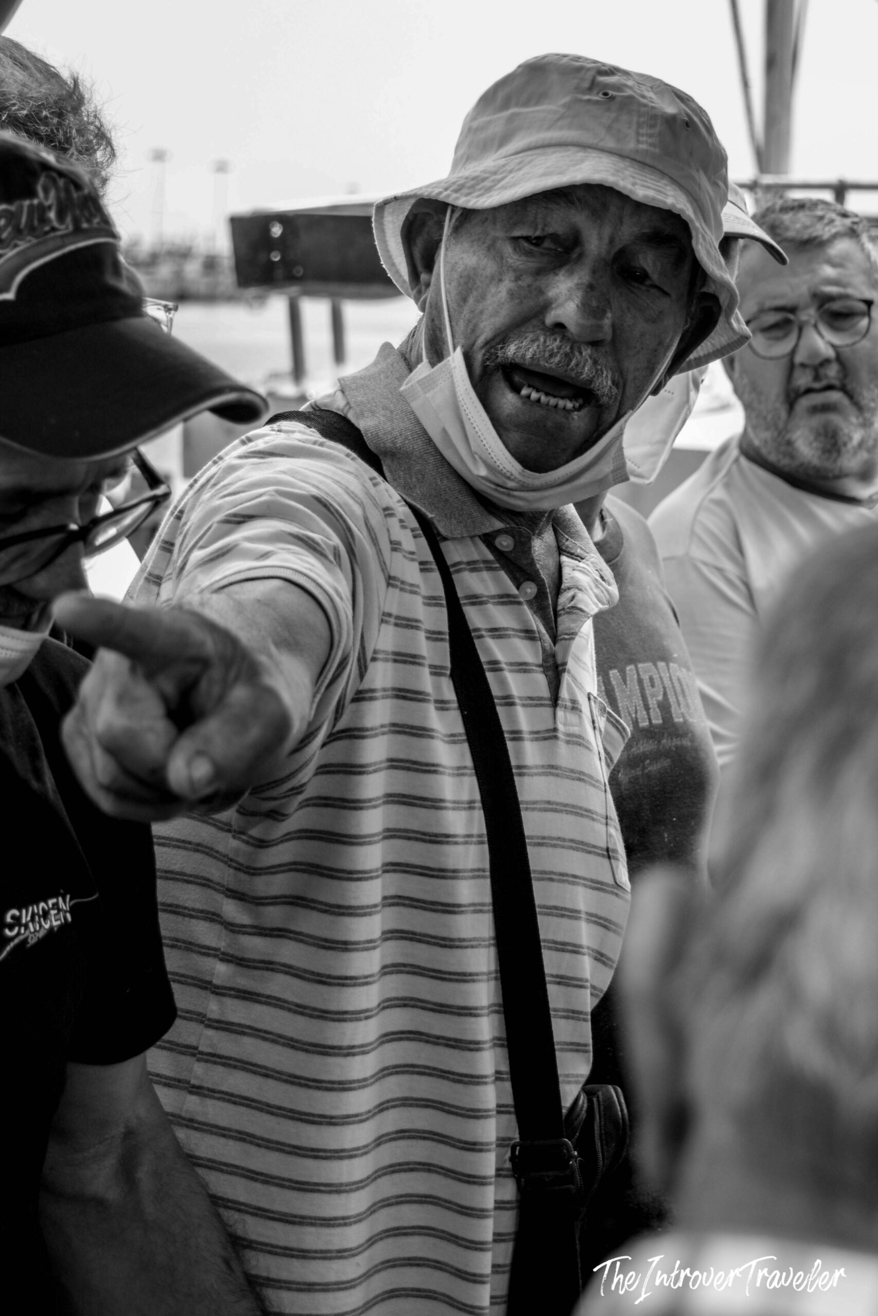 Local fish market vendor wearing a bucket hat, pointing and calling out to customers at a coastal market