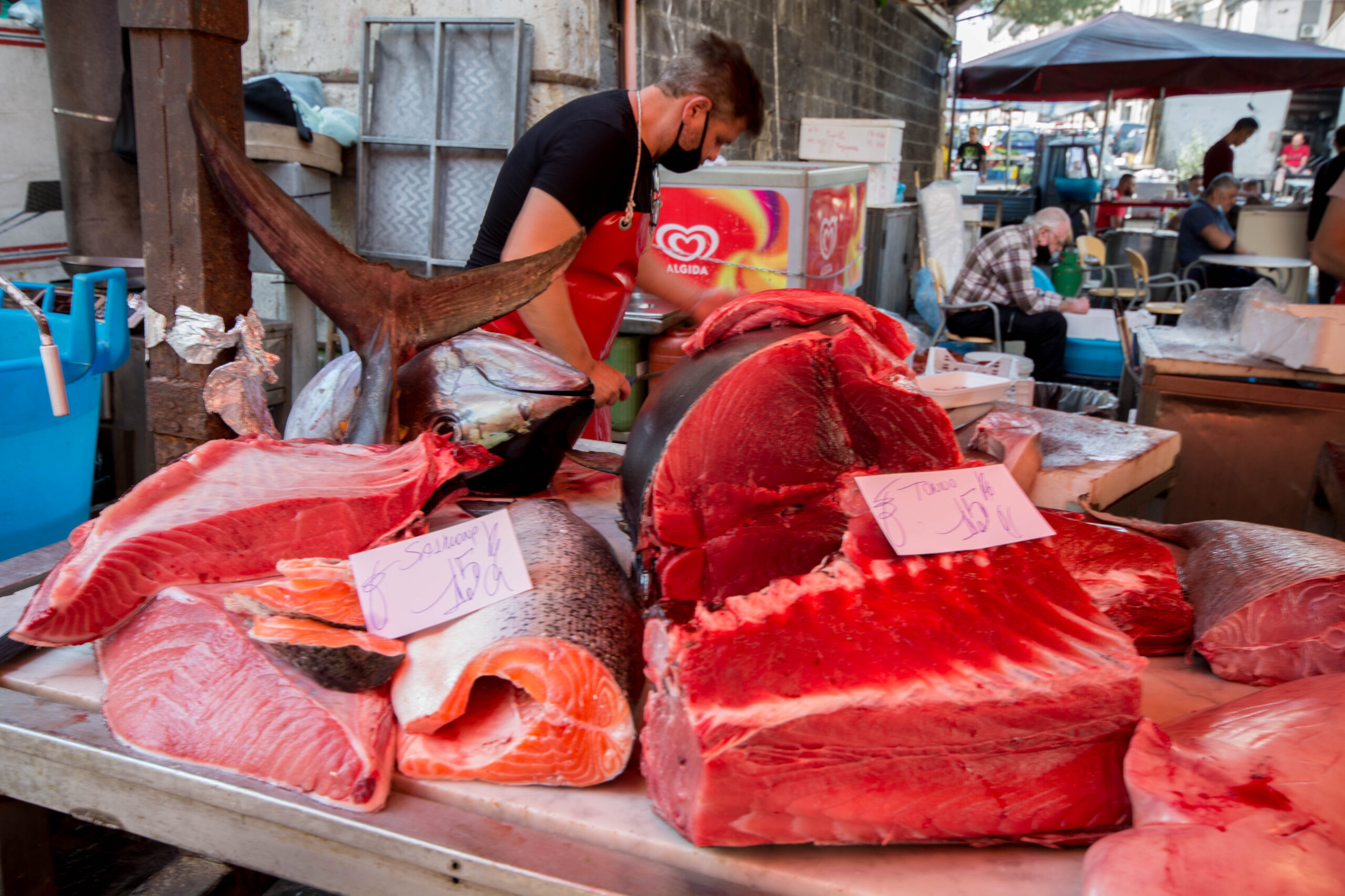 Vendor slicing fresh tuna and salmon at a bustling Sicilian outdoor fish market stall