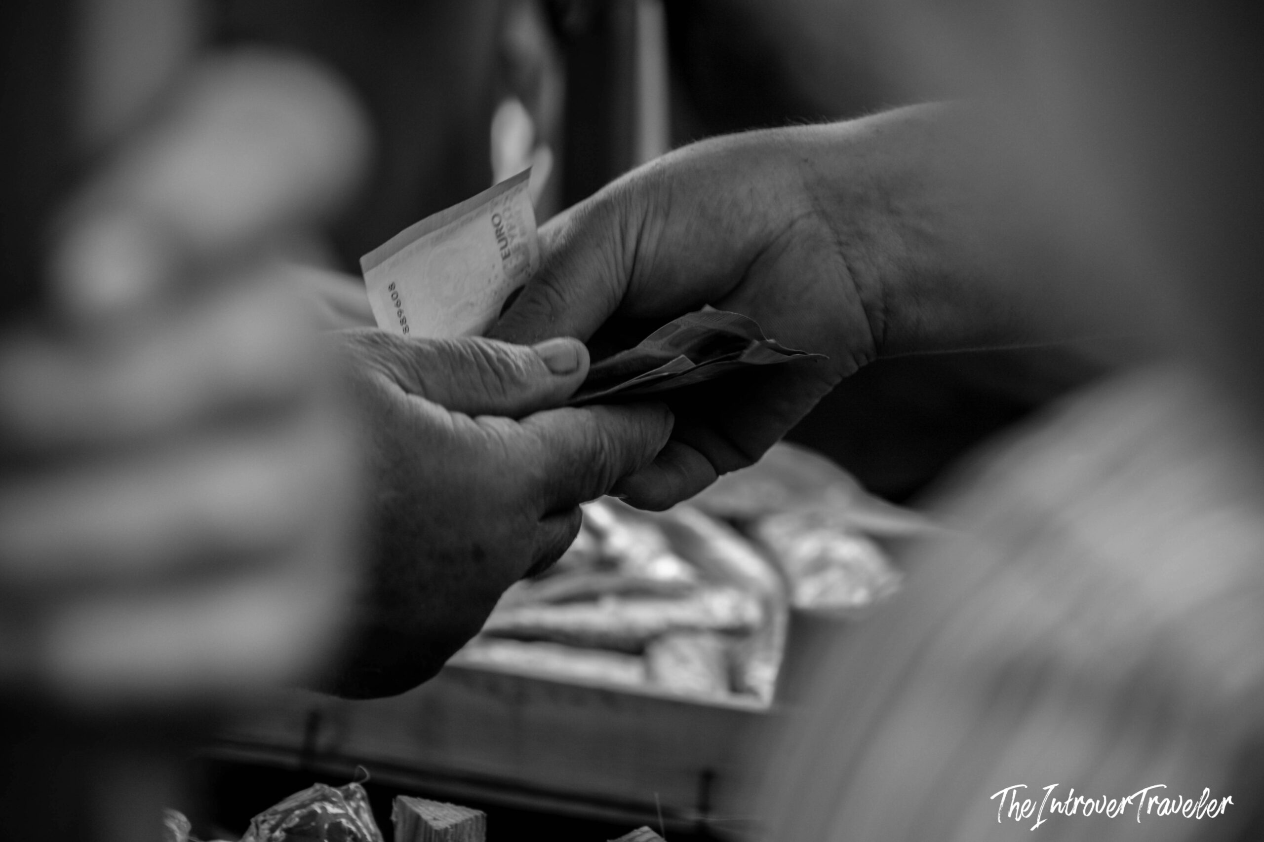 Two hands exchanging euro banknotes at a coastal fish market stall