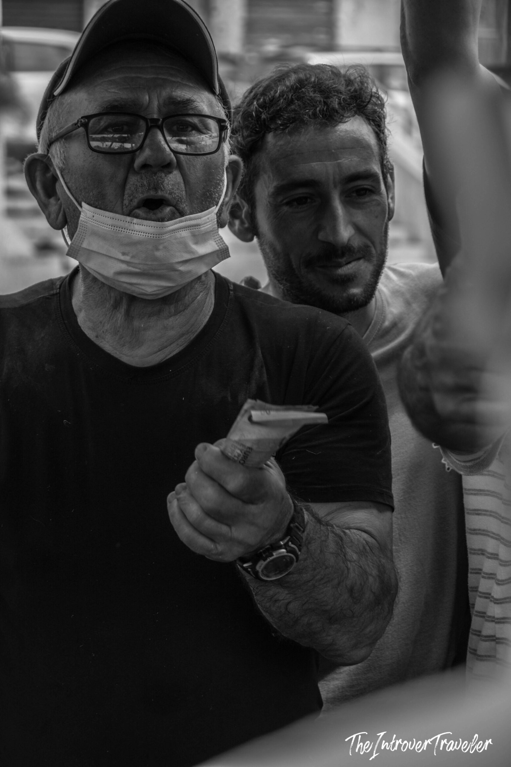 Street vendor with lowered face mask holding cash at a busy coastal city fish market