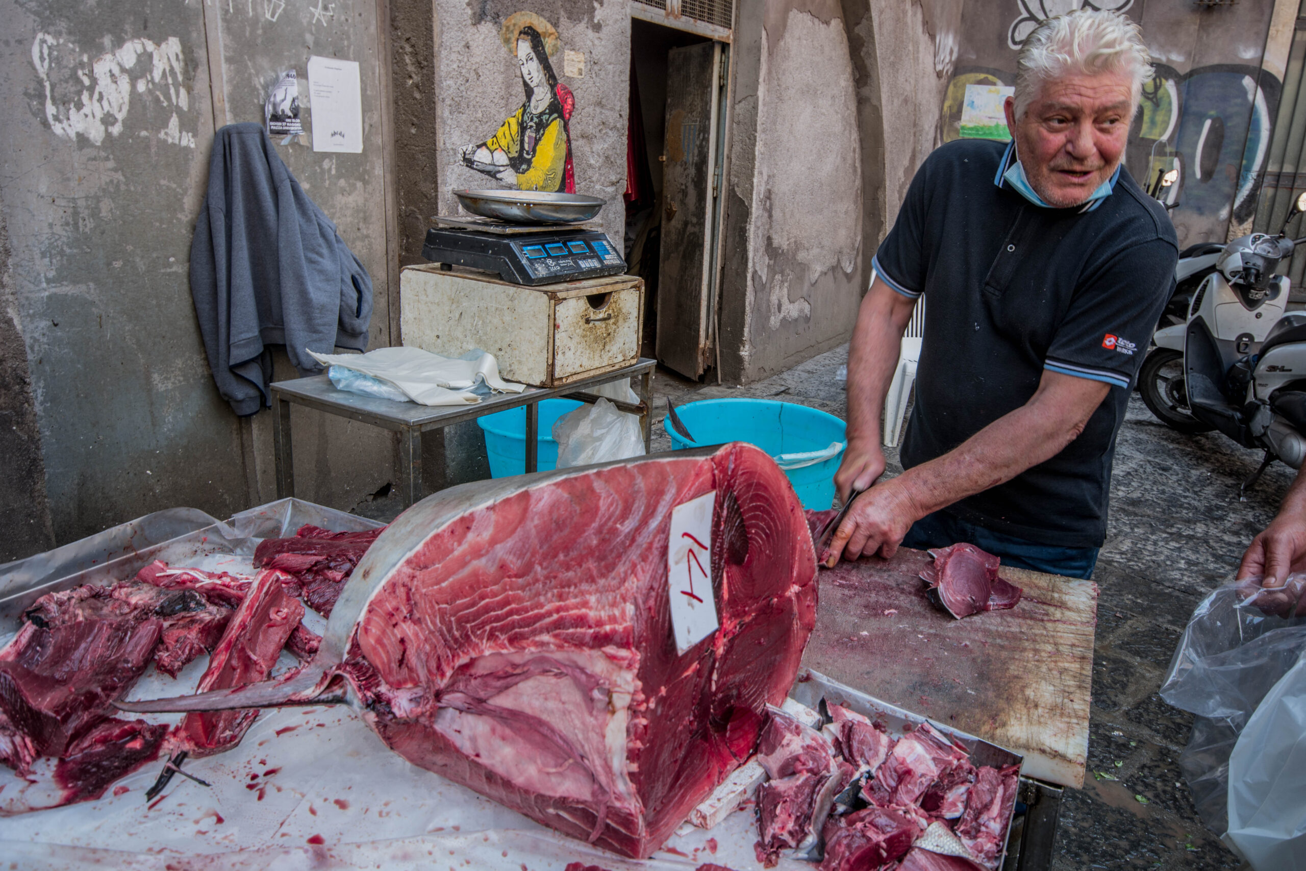 Fishmonger butchering a whole bluefin tuna at a lively coastal city street market