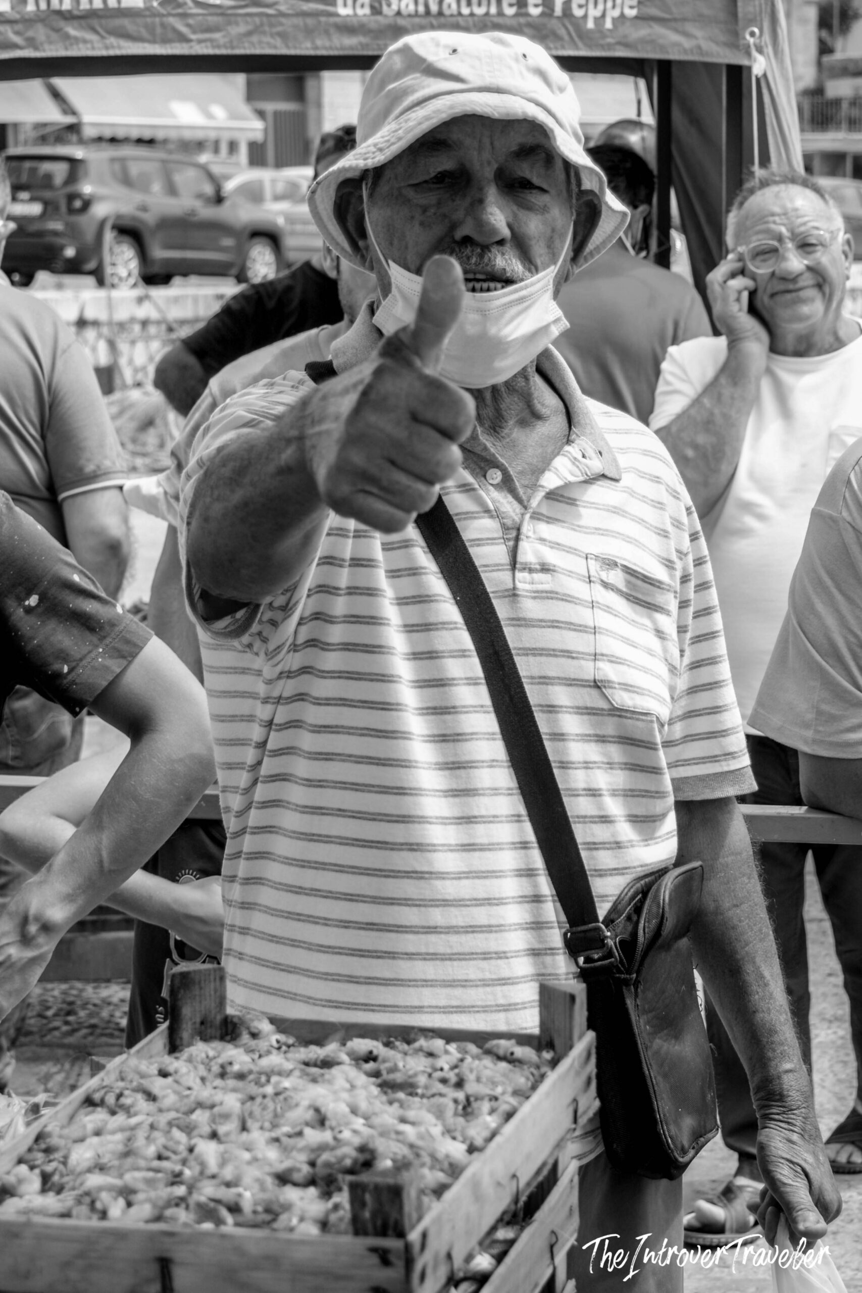 Friendly vendor giving thumbs up at a coastal fish market stall, Italy