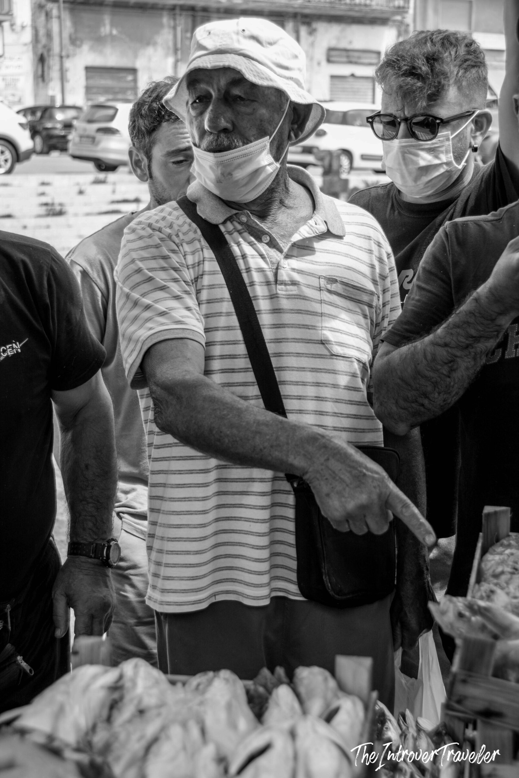 Vendor with face mask pointing at fresh fish at a bustling coastal city market stall