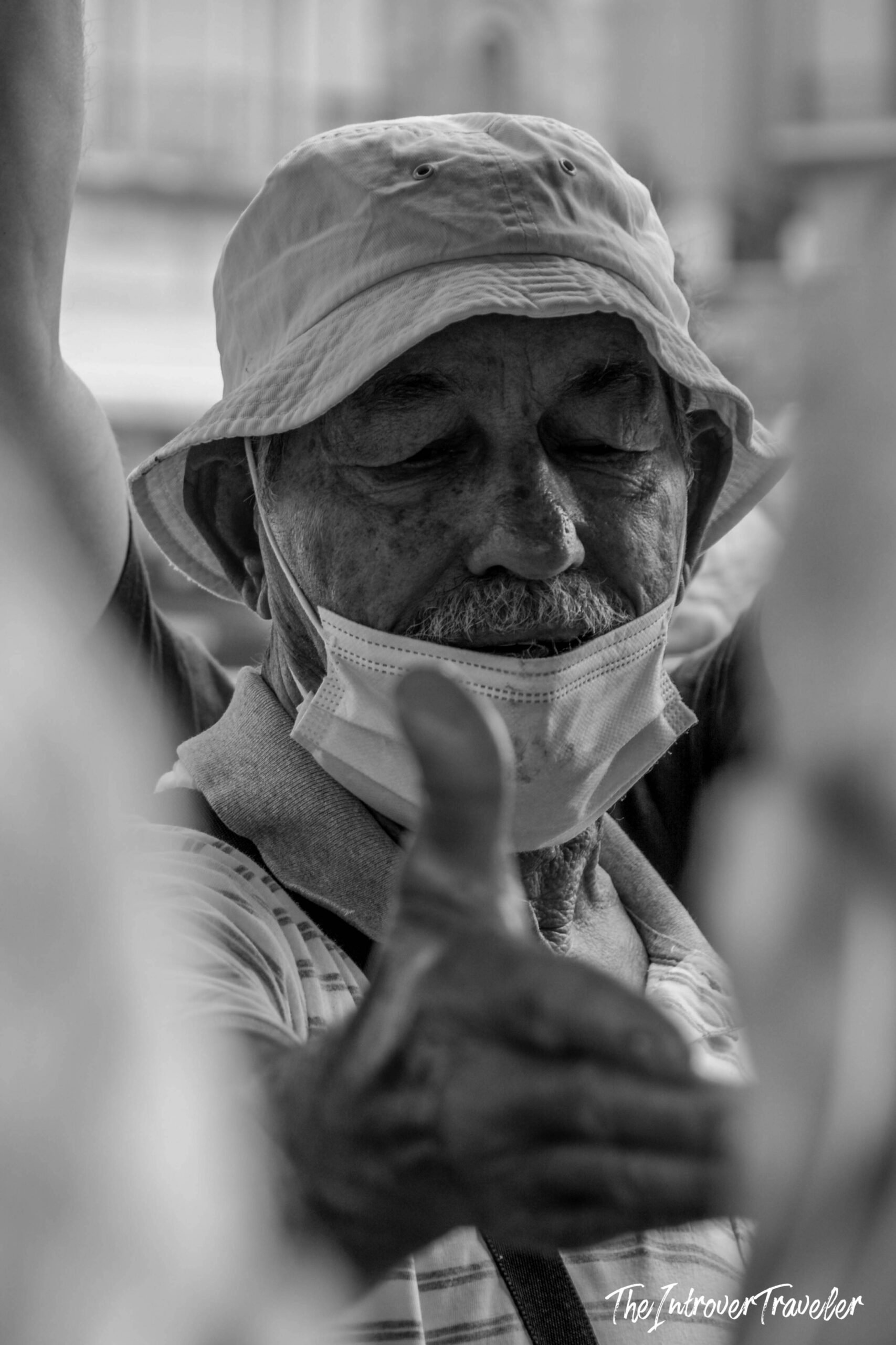 Elderly man in bucket hat and face mask at a bustling coastal city fish market