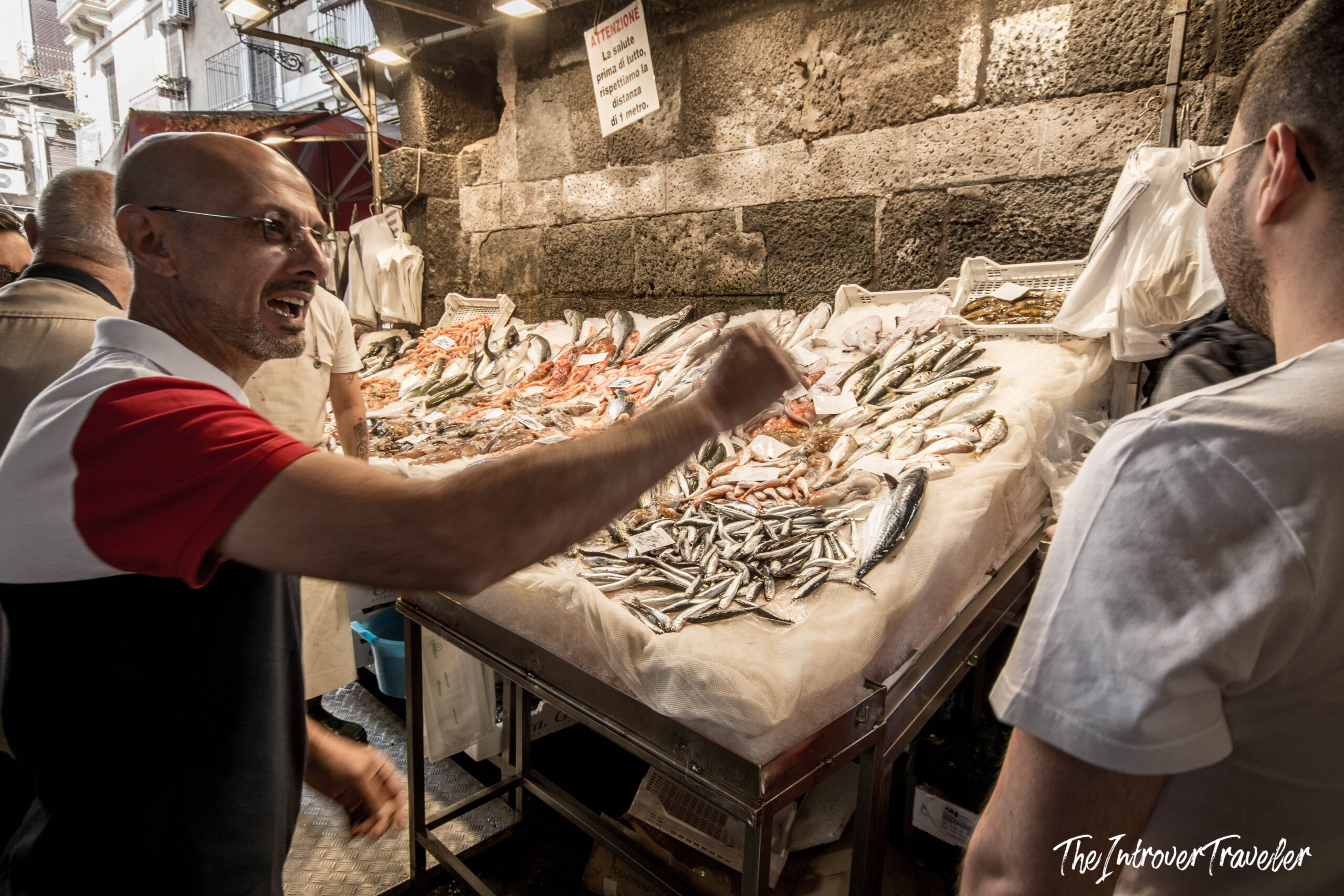 Animated vendor selling fresh anchovies and seafood at La Pescheria fish market in Catania, Sicily