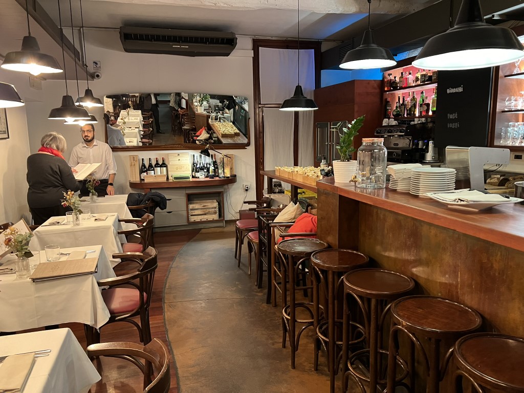 Interior of Parlor Bologna, a cozy trattoria with bentwood chairs, white tablecloths, and a warm wooden bar counter.