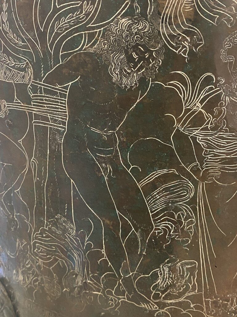 Close-up of an engraved bronze Etruscan artifact at Villa Giulia, showing a bearded male figure with foliage