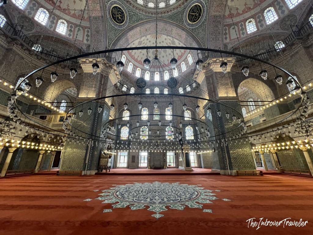 Interior of the New Mosque (Yeni Cami) in Istanbul, with ornate domes, Iznik tiles, and circular chandeliers