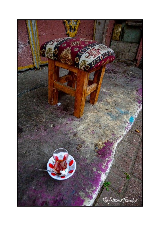 Turkish tea glass on a saucer beside a kilim-topped stool at an Istanbul street cafe