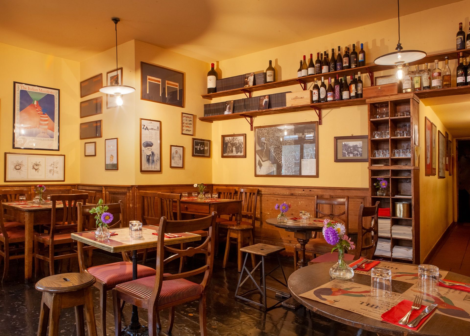 Warm interior of Trattoria Cibrèo Florence, with wooden chairs, wine shelves, and vintage art posters
