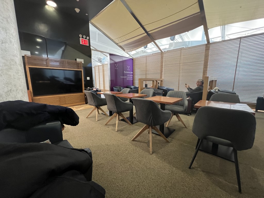VIP One Lounge JFK seating area with gray chairs, wood tables, and purple branded signage
