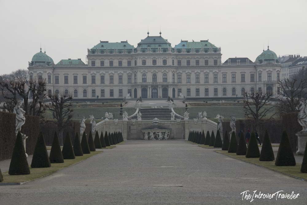 Upper Belvedere Palace in Vienna, seen from the formal French-style garden pathway lined with cone-shaped topiaries and baroque sculptures