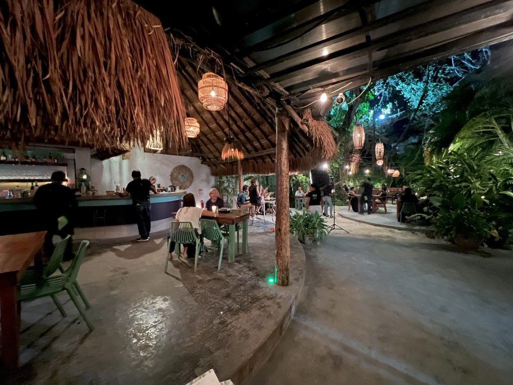 Kondesa Cozumel open-air dining area at night, with palapa roof, wicker lanterns, and jungle surroundings