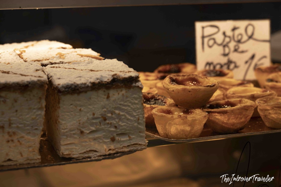 Pastel de nata tarts priced at 1 euro in a Porto bakery display case, beside a cream cake
