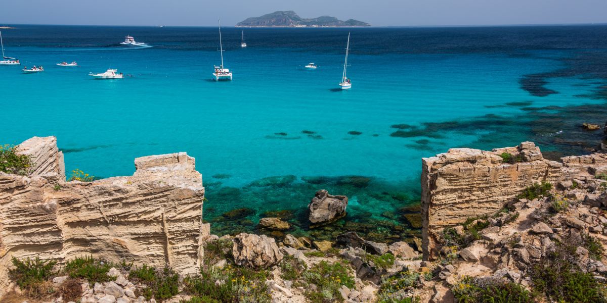 Turquoise waters of Favignana, Egadi Islands, with sailboats anchored near layered limestone cliffs