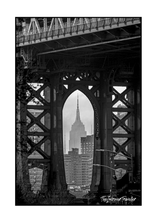 Empire State Building framed through Manhattan Bridge arch, black and white New York street photography