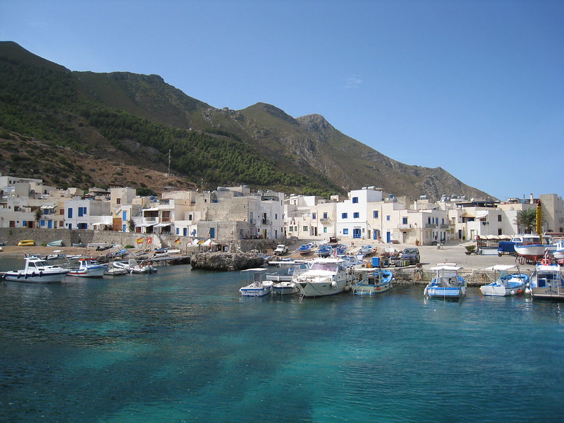 Marettimo harbor, turquoise waters and white cubic houses below rocky hills, Egadi Islands Sicily