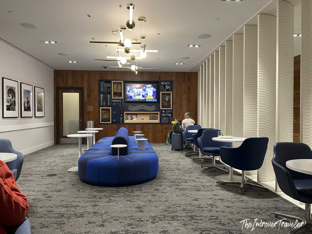 Seating area inside the Amex Centurion Lounge at LGA, with blue sofas, navy chairs, and a TV wall display