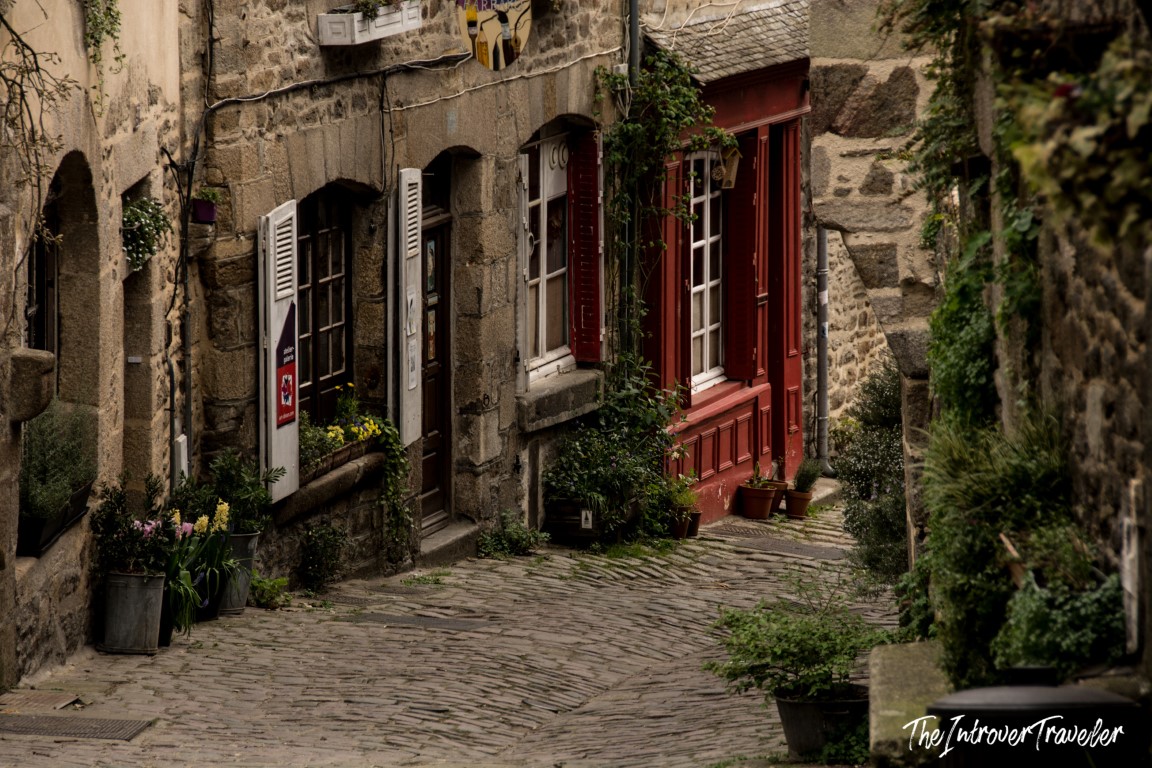 Cobblestone street in Dinan, Brittany, lined with medieval granite buildings and red-shuttered shops