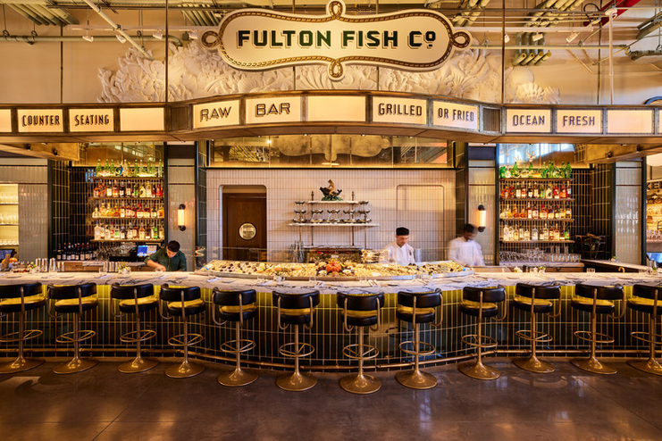 Fulton Fish Co raw bar counter at Pier 17, with gold bar stools, tiled facade, and fresh seafood display