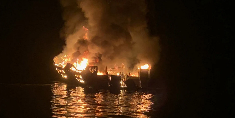 Dive boat engulfed in flames on dark water at night, illustrating shipwreck fire risk for scuba divers