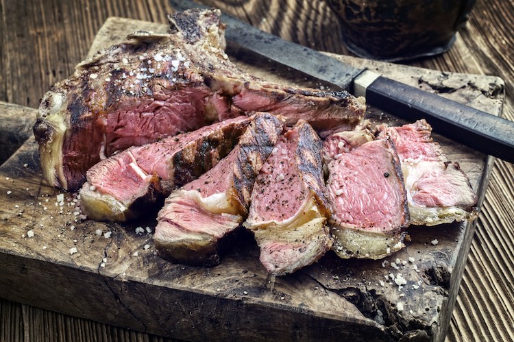 Bistecca alla Fiorentina, sliced T-bone steak on a rustic wooden board, a Tuscan cuisine classic
