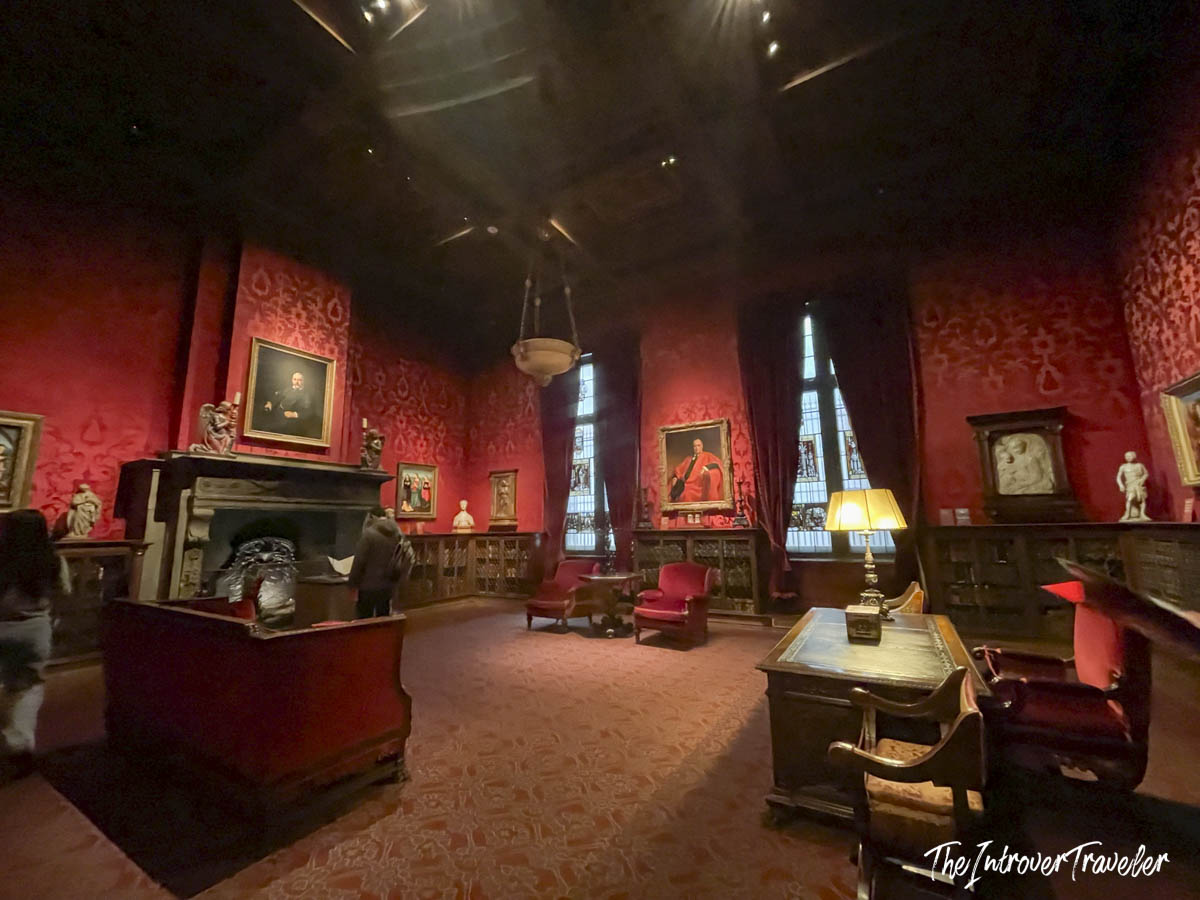 Dimly lit red damask study room at the Morgan Library, displaying Renaissance sculptures and portrait paintings