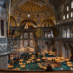 Interior of Hagia Sophia Istanbul, showing the vast domed nave, Islamic calligraphy medallions, and chandelier-lit prayer hall