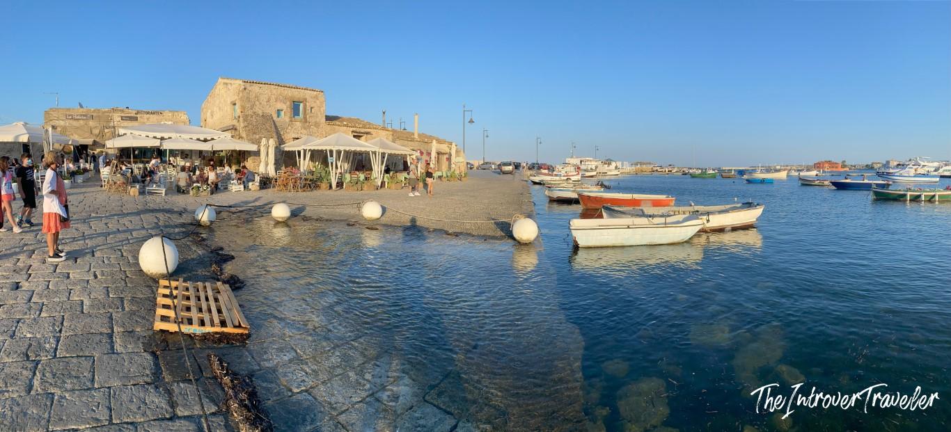 Marzamemi harbor in Sicily, with fishing boats, waterfront restaurants, and stone buildings at golden hour
