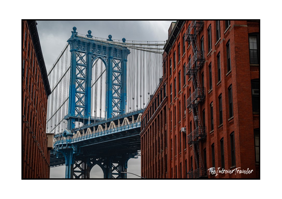 Manhattan Bridge tower framed by red brick DUMBO warehouses, iconic New York street photography view
