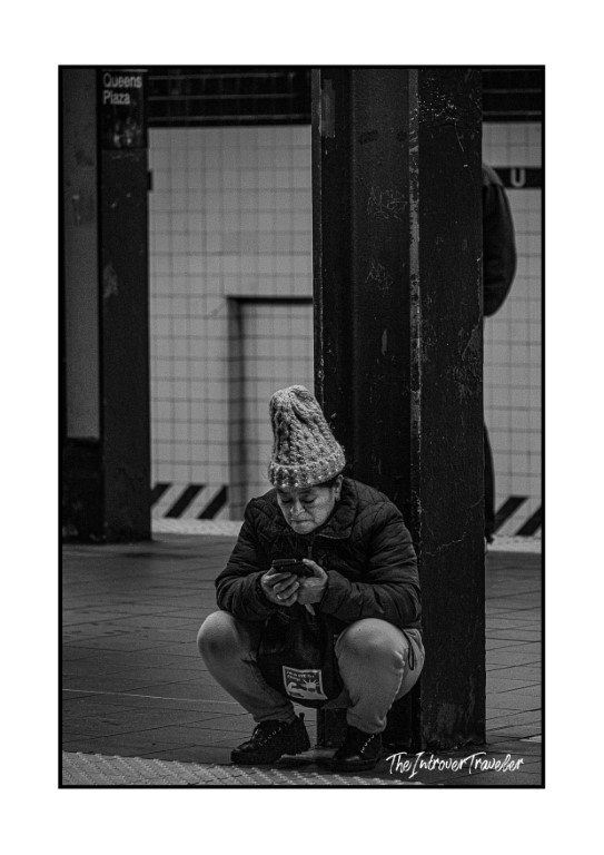 Person crouching with phone at Queens Plaza subway station, NYC street photography