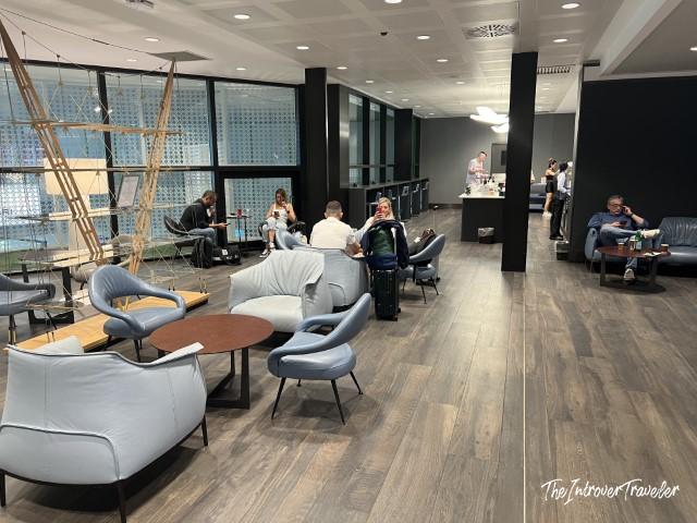 Interior seating area of the Leonardo Lounge at Milan Linate Airport, with blue armchairs and a bar counter