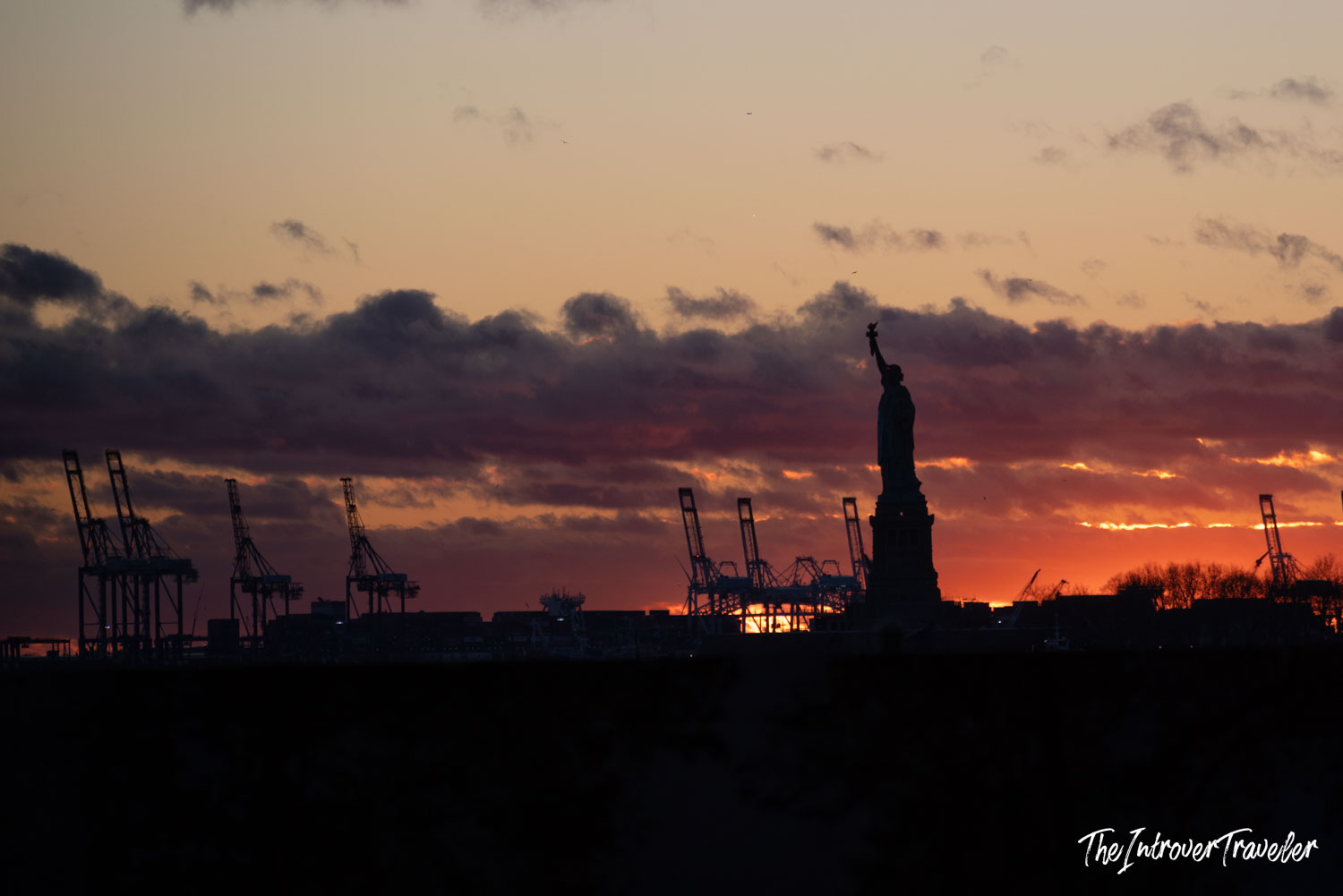Statue of Liberty silhouette against a fiery red and orange sunset over New York Harbor