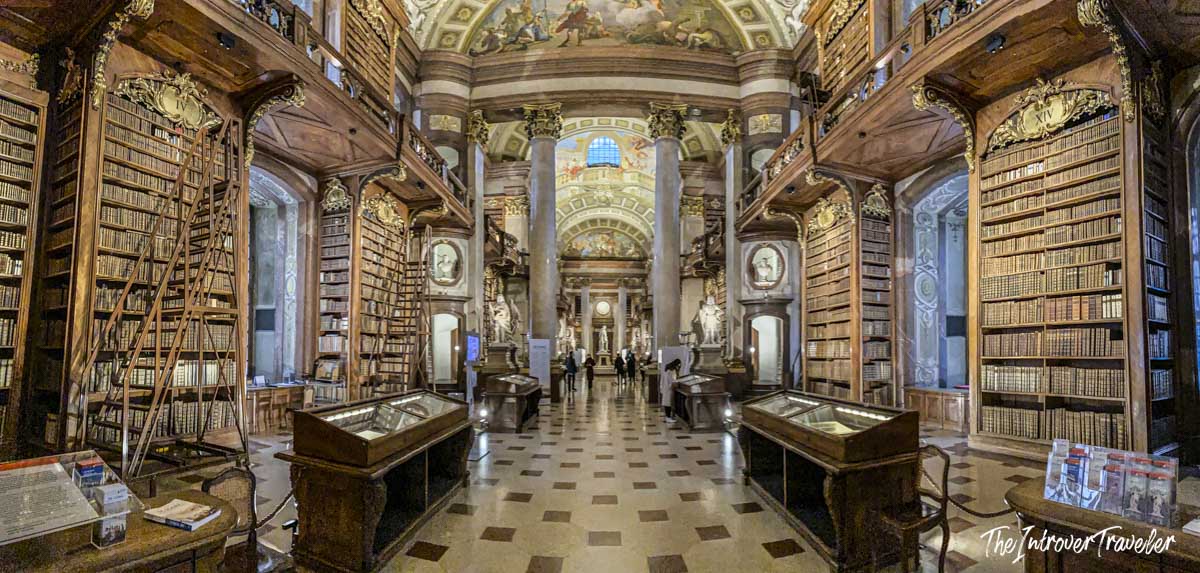 Panoramic view of the Austrian National Library State Hall in Vienna, with baroque frescoed ceilings and towering bookshelves