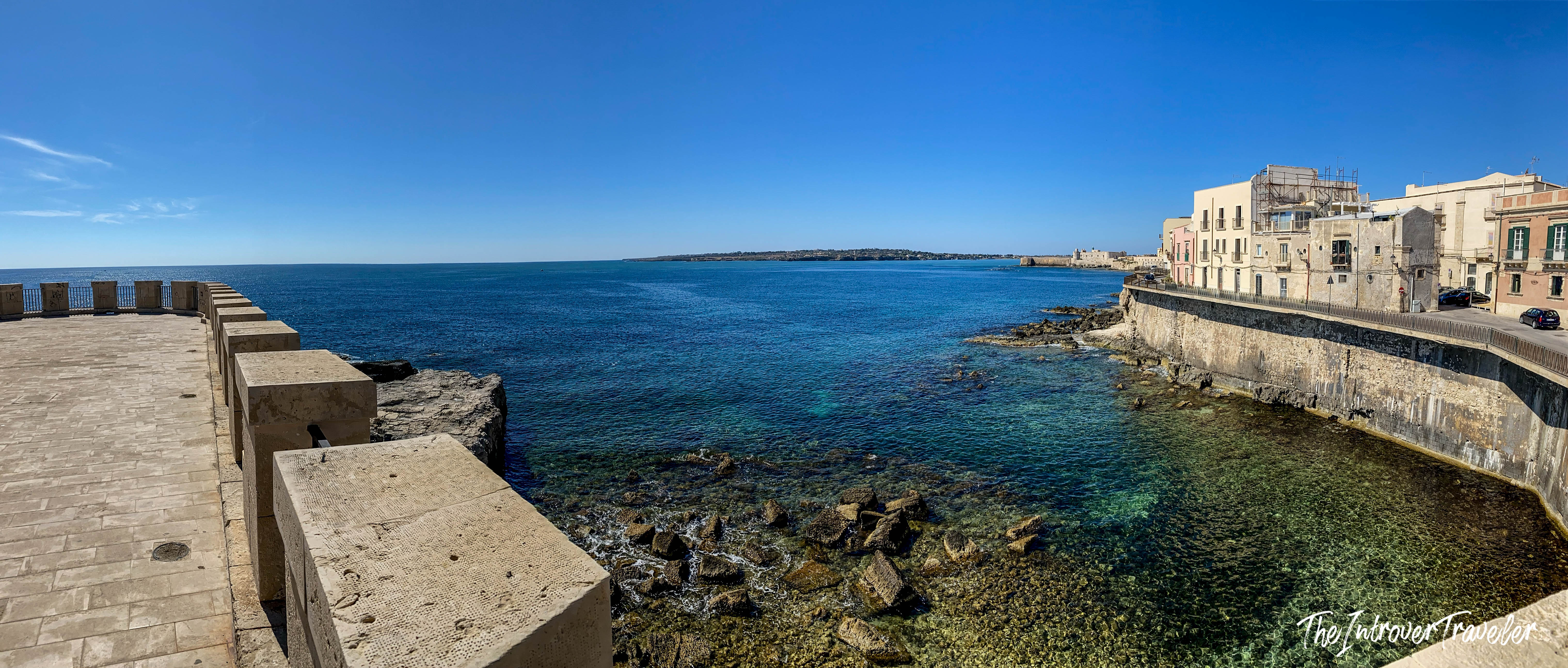 Panoramic view of Ortigia island coastline, Syracuse, with crystal-clear Mediterranean waters and historic seafront buildings