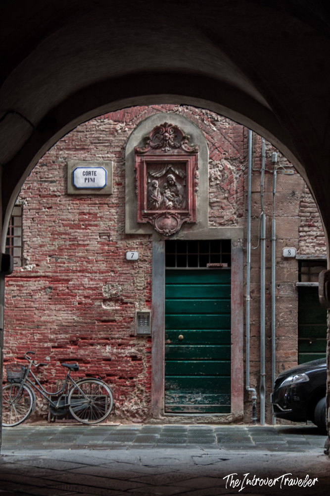 Corte Pini alley in Lucca, framed by an arch with a Madonna relief above a green door