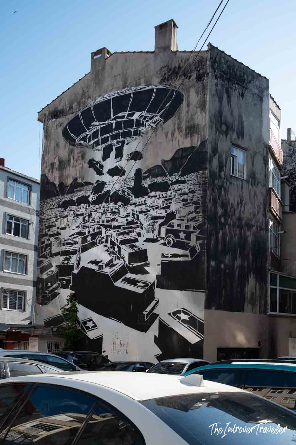 Large black and white street art mural in Kadıköy, Istanbul, showing a UFO beam lifting military vehicles