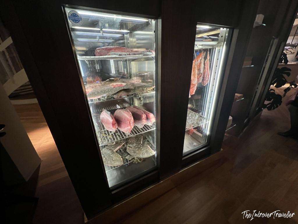 Glass display fridges at a Rimini seafood restaurant, showing fresh fish, crabs, and cured meats on shelves
