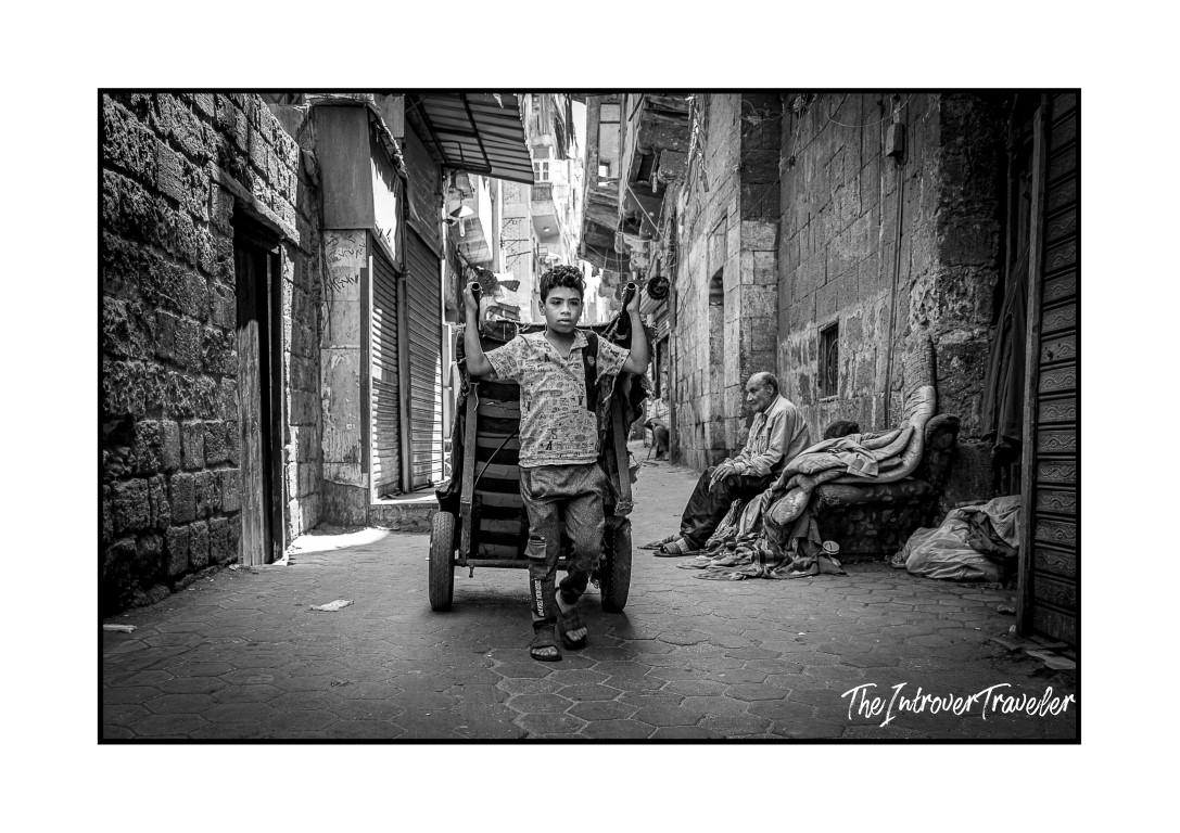 Boy pulling a cart through a narrow Cairo alley, black and white street photography in Egypt